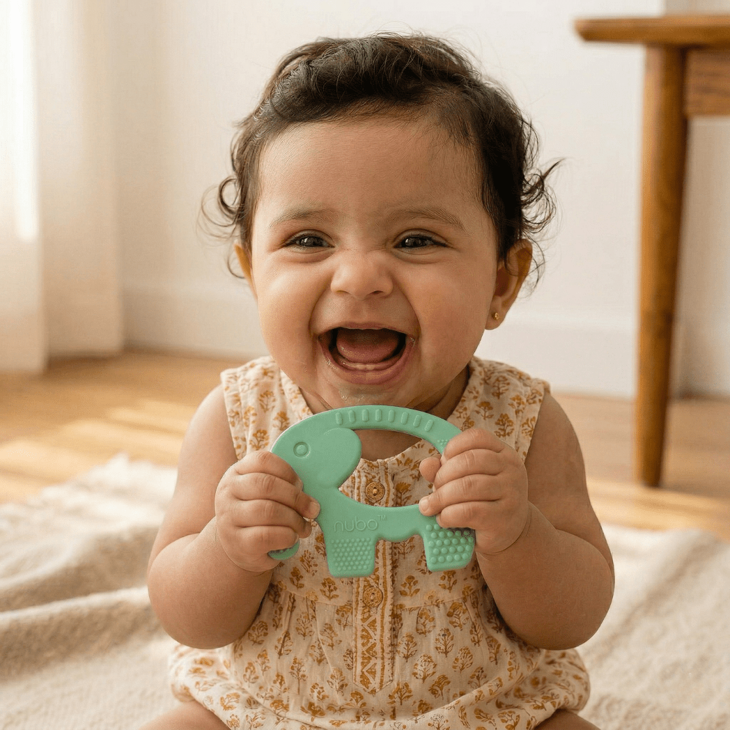 Baby holding a green ele ring teether with a neutral background